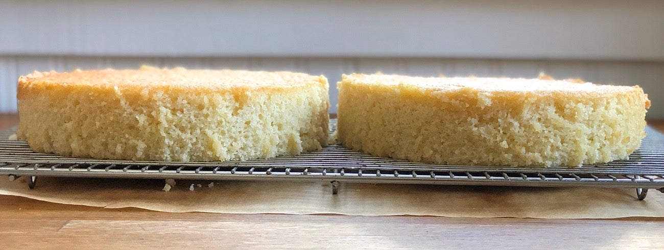 Two cake layers on a cooling rack, side by side, waiting to be frosted.